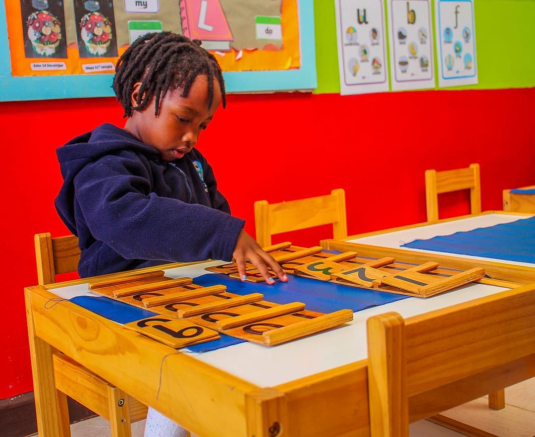 A child tracing Montessori sandpaper letters laid out on a work mat